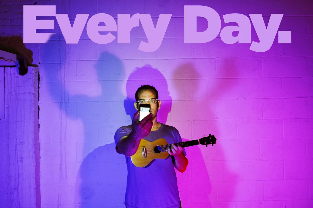 Jonathan Mann playing ukulele beneath an Every Day sign
